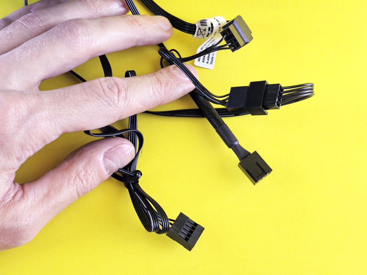 services-02 A hand holding black computer cables against a bright yellow background, showcasing technology connection.